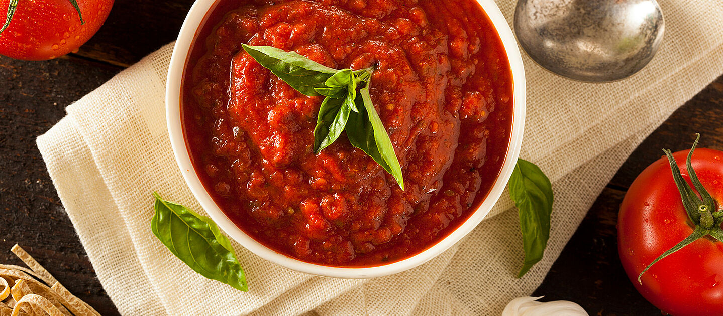 A white bowl with tomato soup and basil.