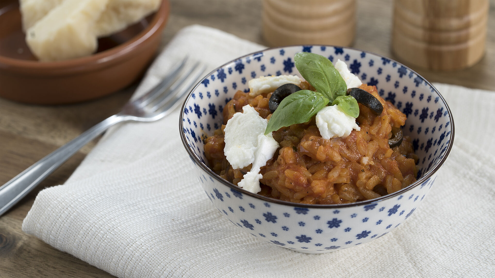 Tomato risotto with olives and basil in a blue and white bowl.