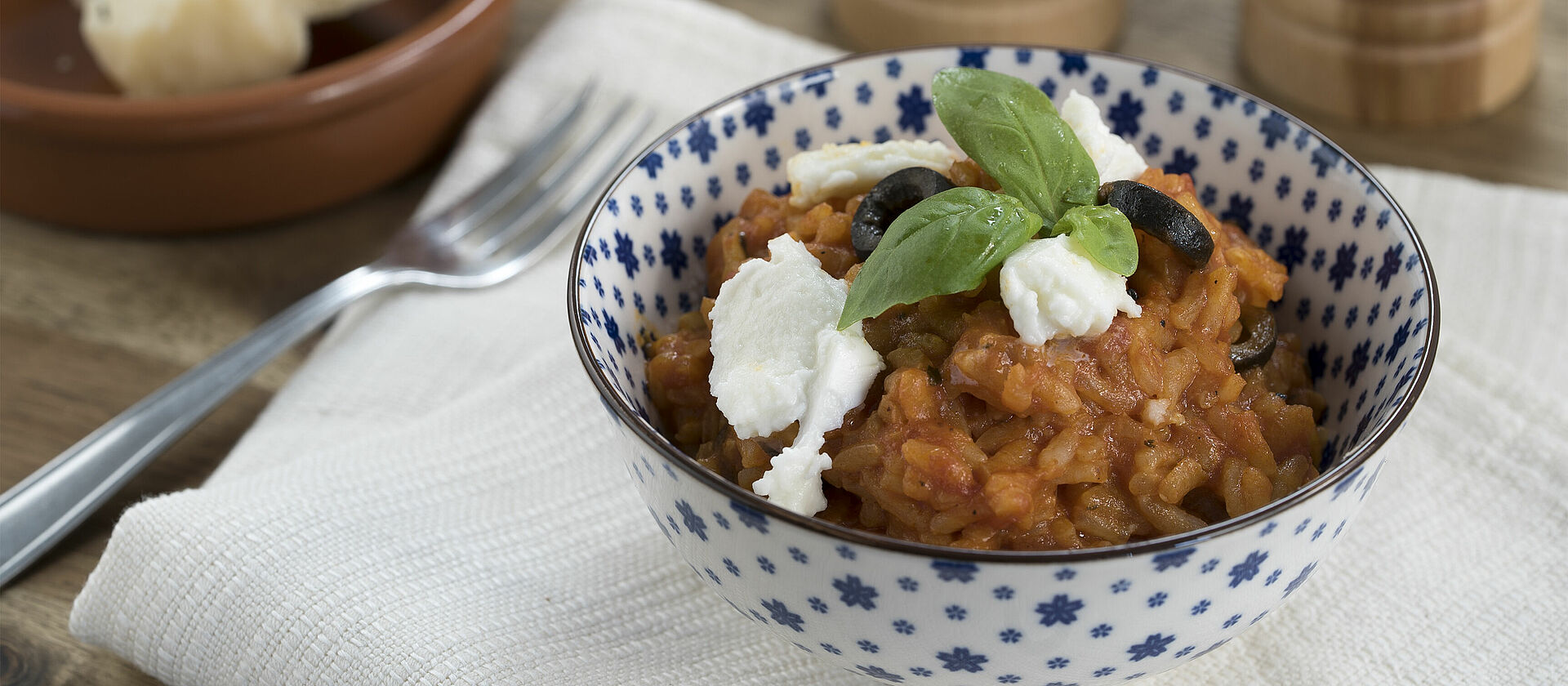 Tomato risotto with olives and basil in a blue and white bowl.