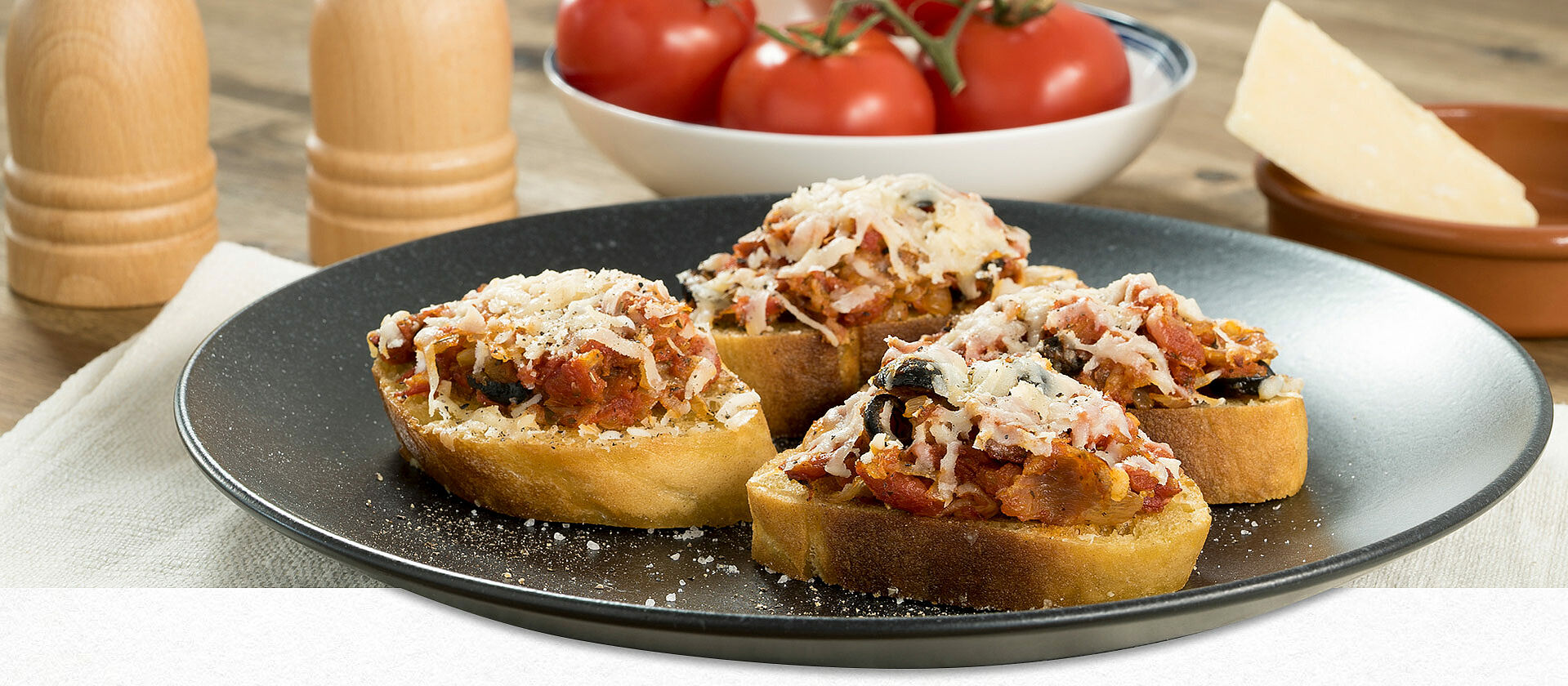 Four bread slices with bruschetta on a black plate.