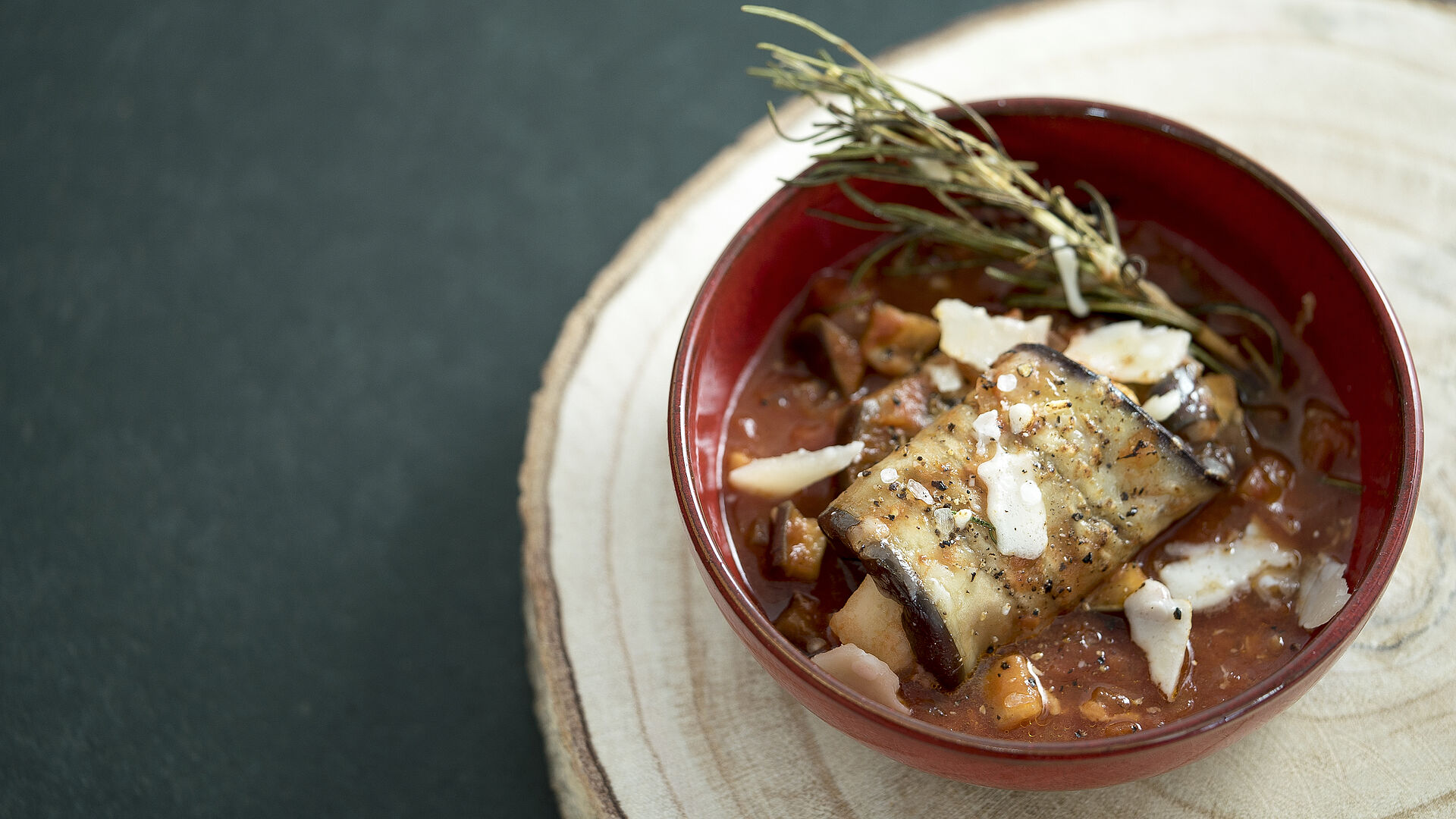 Braised eggplant rolls in a red bowl.