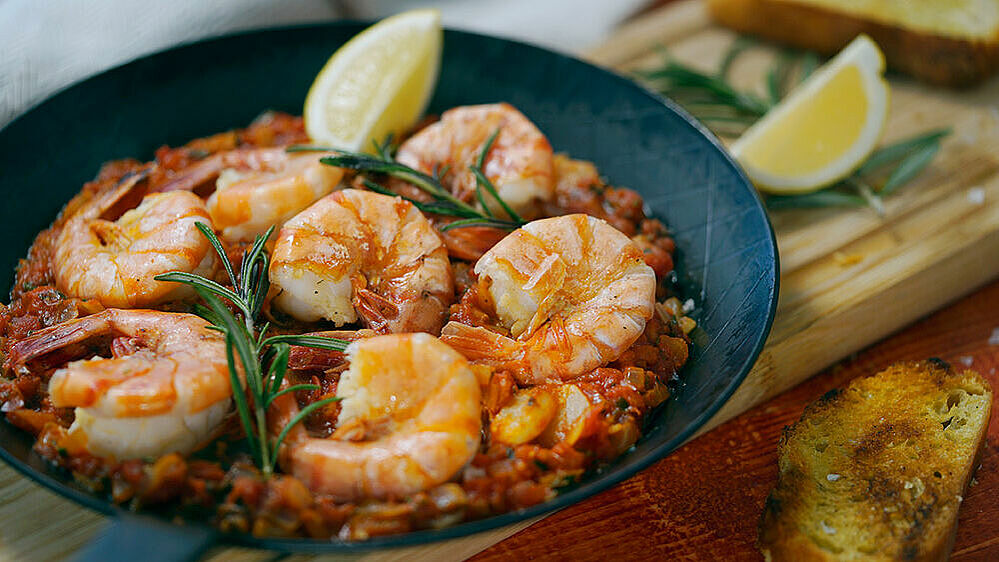 King prawns with tomato sauce, a lemon quarter and rosemary arranged on a plate