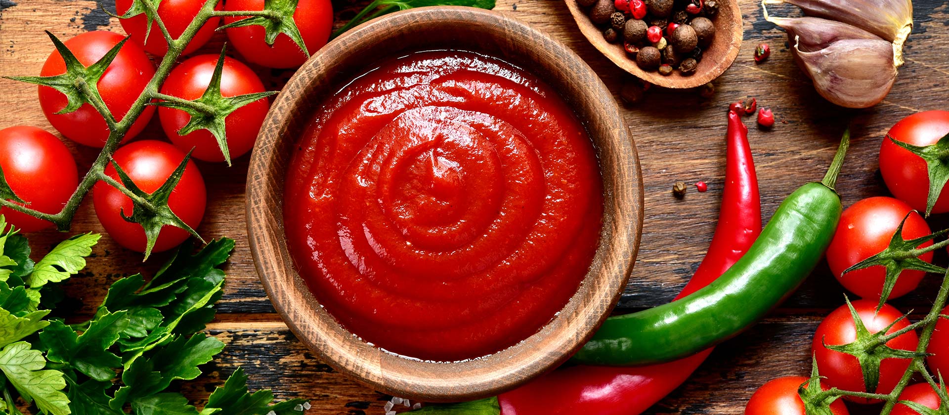 Passierte Tomaten in einer Holzschüssel auf einem Tisch mit frischen Zutaten. 