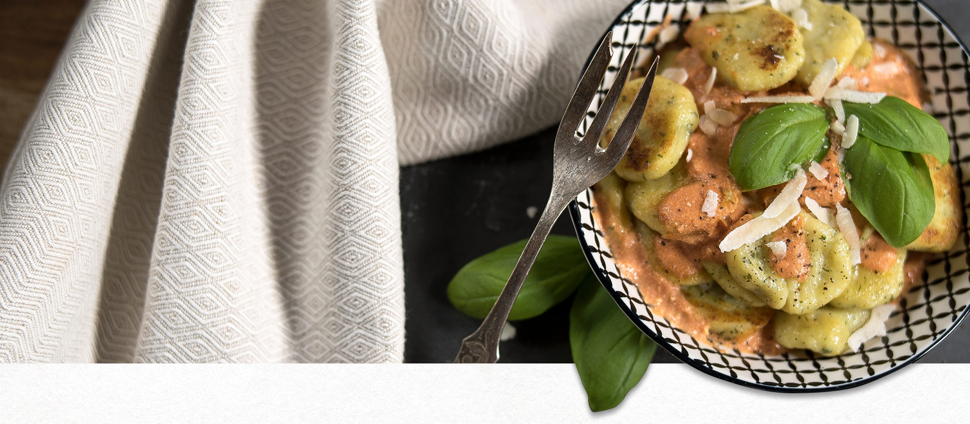 Basil gnocchi in a black and white bowl next to a cloth.